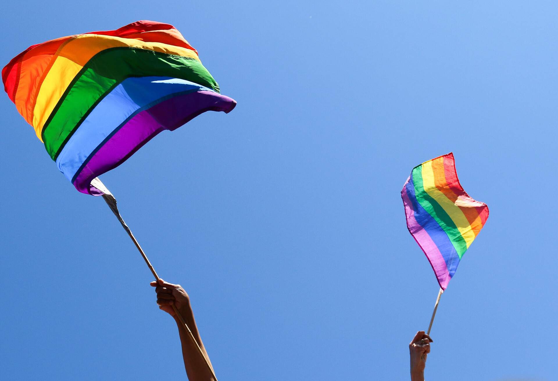 Pride flags raised into the blue sky by two hands.