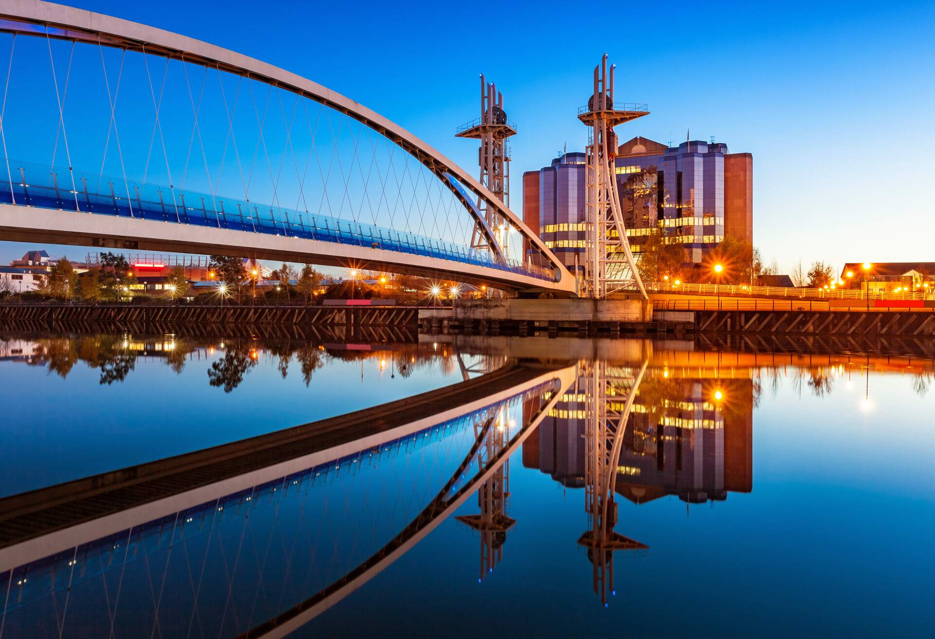 A modern arched steel bridge above the river and a building with a modern and classic look.