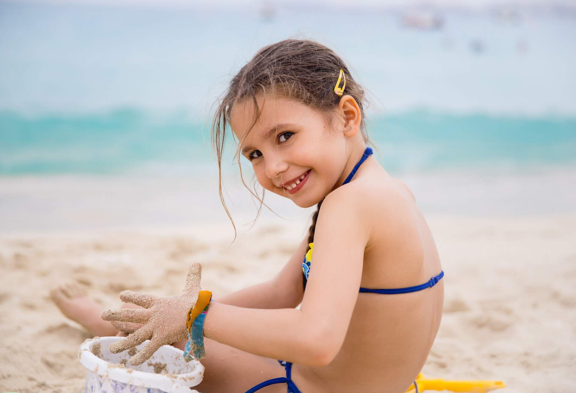 A little girl in her bikini is playing on the sand.