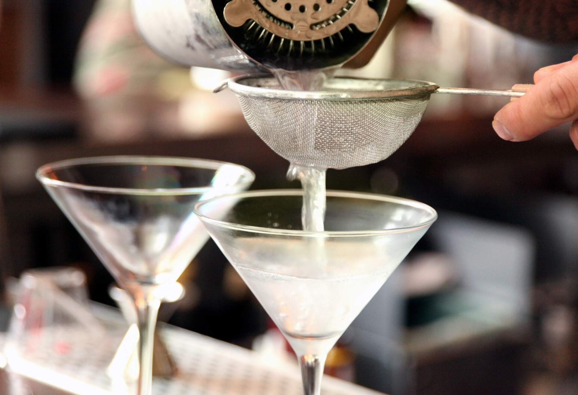 a bartender pouring martinis into chilled glasses through a small wire mesh strainer.