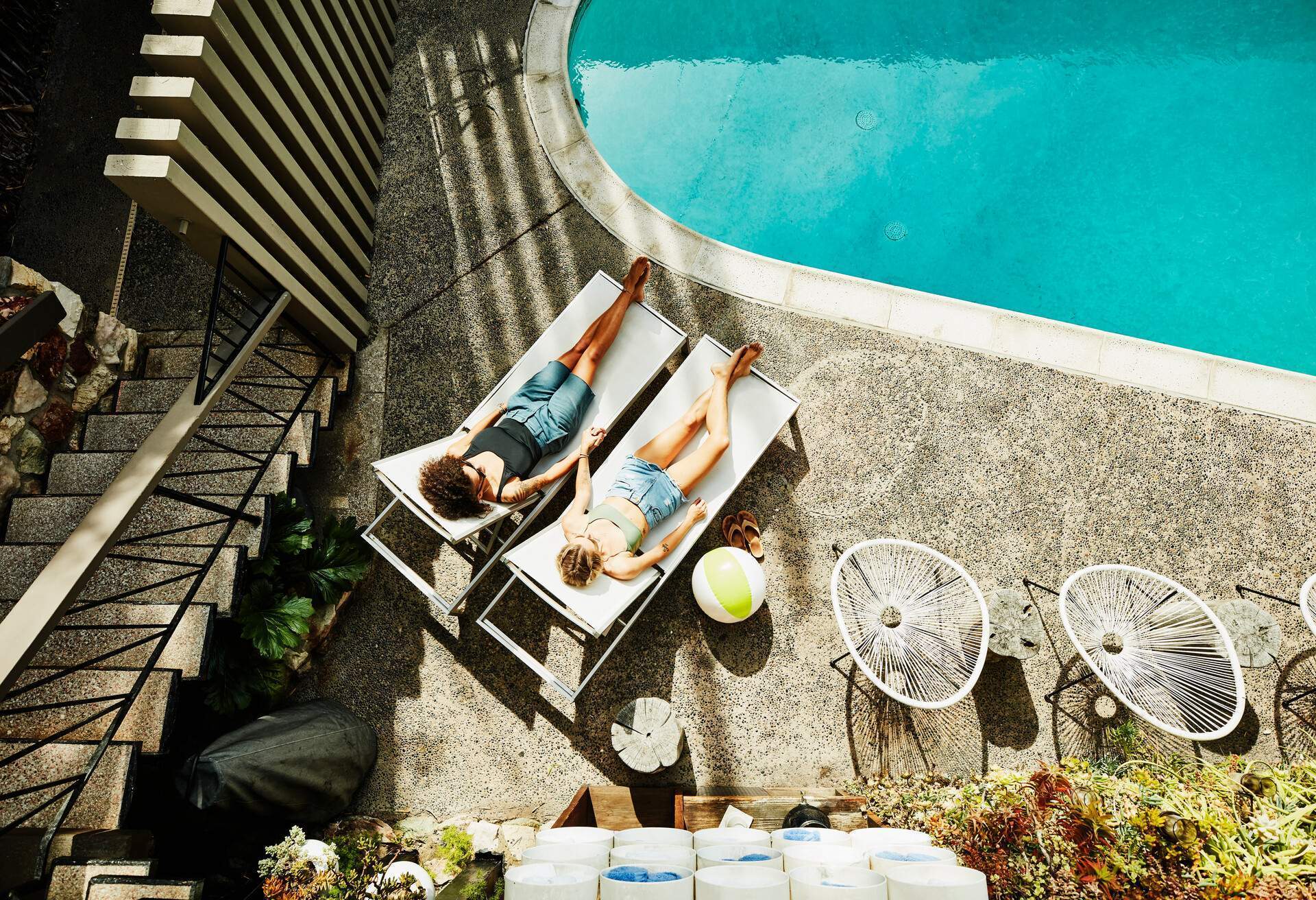 Two women holding hands as they sit on lounge chairs by the pool.