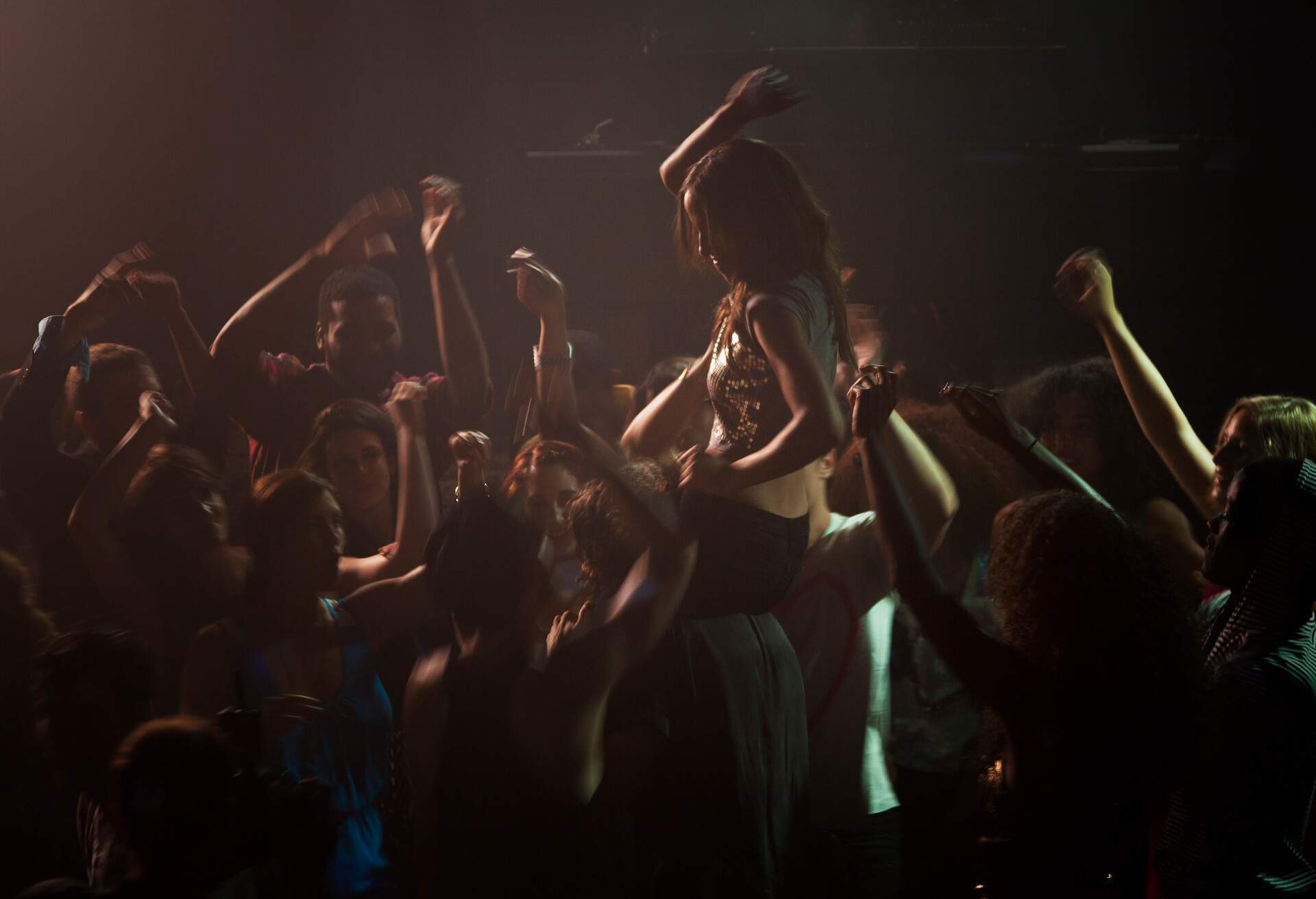 People on the dancefloor of a nightclub cheering around a woman over a man's shoulder.