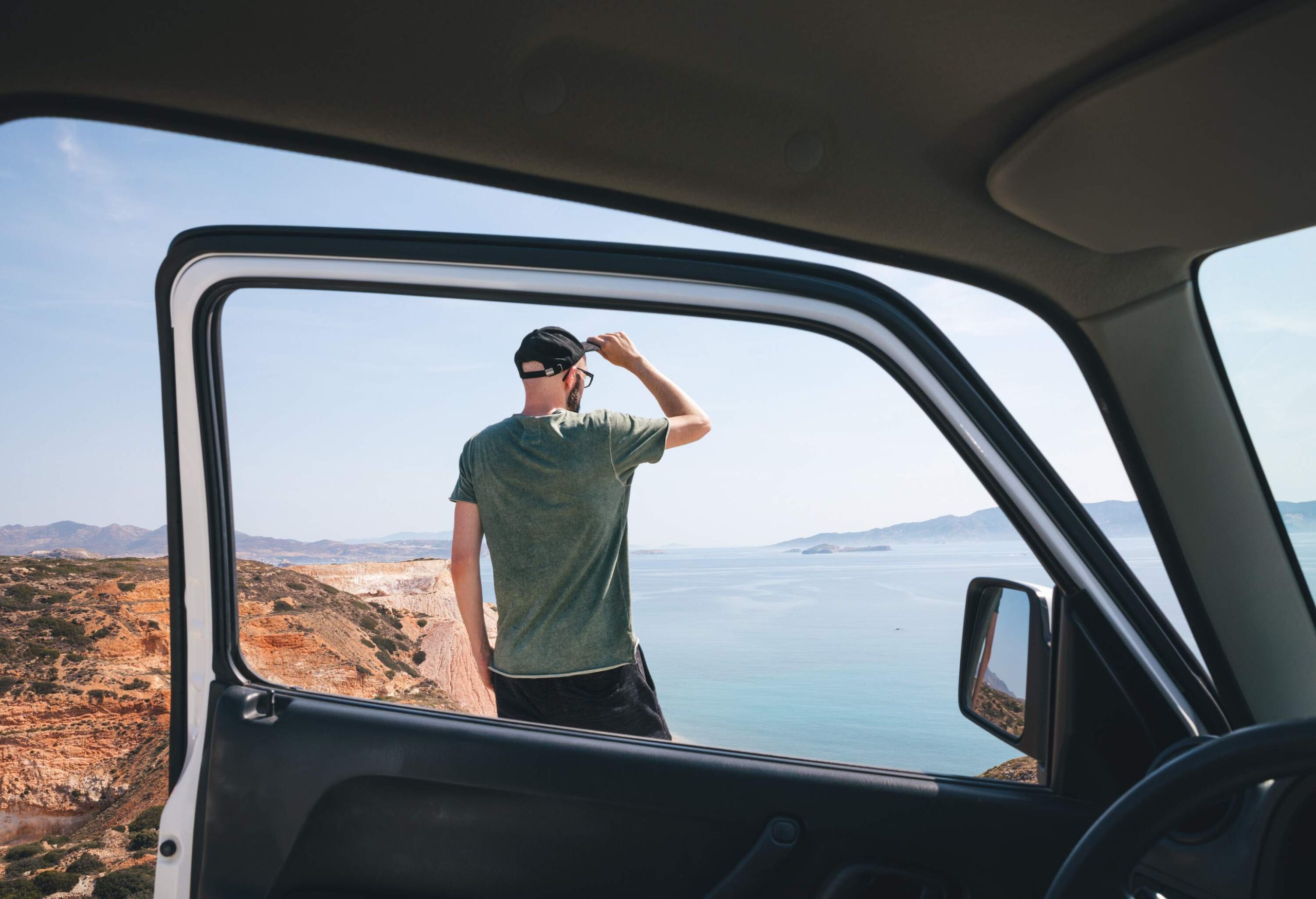 A man standing outside of his parked car with the door open, looking out over the landscape.