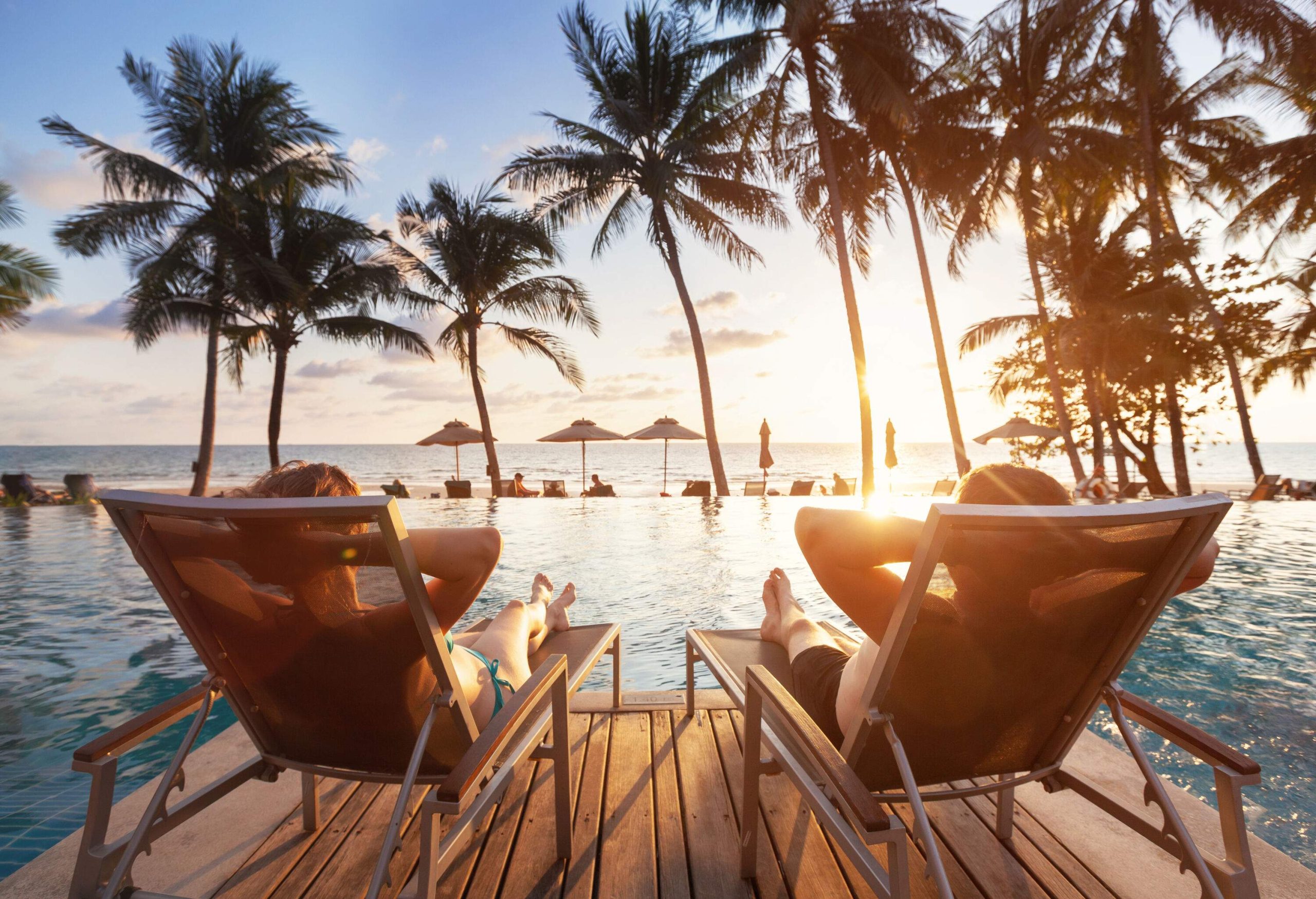 Couple relaxing on the sun loungers on the wooden deck by the pool and enjoying the sunset and sea.