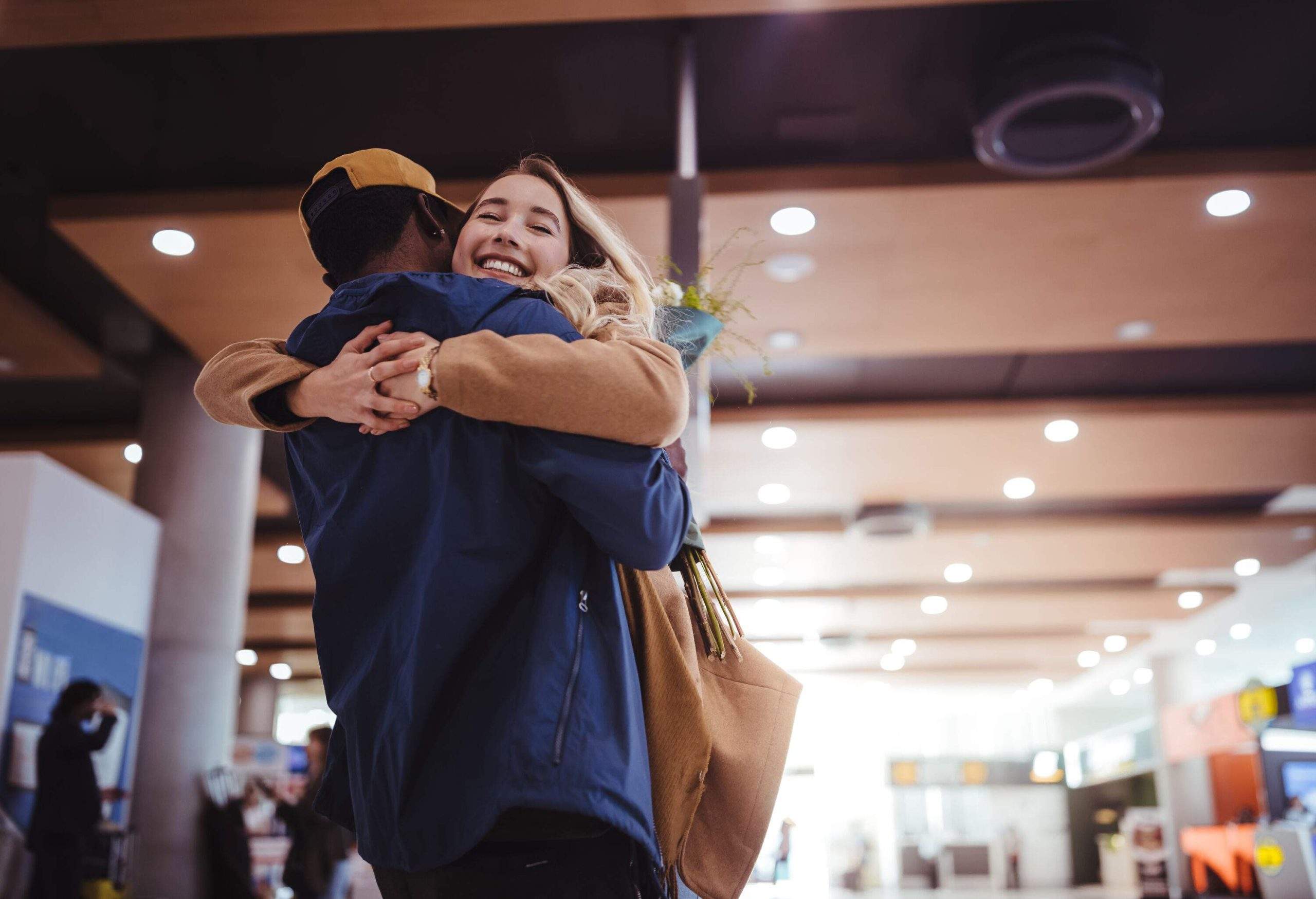 A joyful multi-ethnic couple excitedly reunites and embraces each other in the bustling atmosphere of an airport.