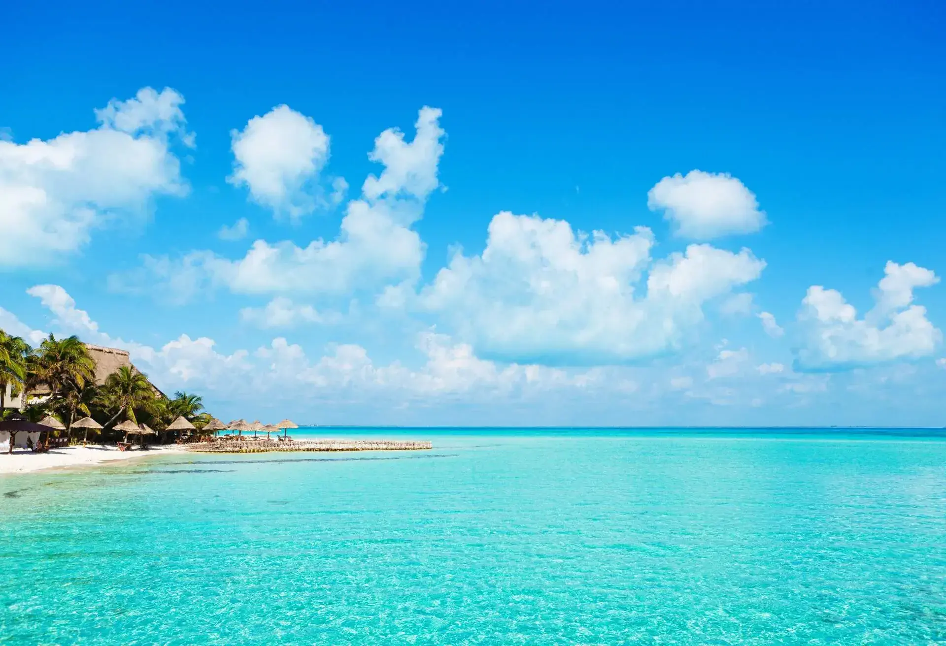 Subject: Horizontal view of the vacation resort hotel on the island of Isla Mujeres, with pristine white sandy beach that face the gentle waves of the aqua blue Caribbean Sea in the glow of morning sunlight.