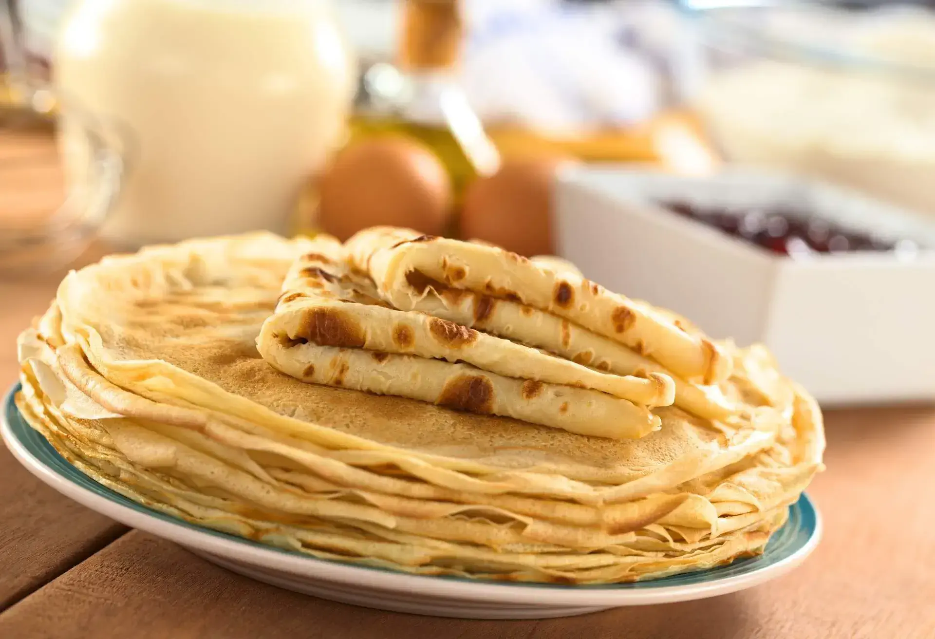 Fresh homemade crepes on plate with ingredients and strawberry jam in the back (Selective Focus, Focus on the front edge of the lower folded crepe); Shutterstock ID 103657649; Purpose: ; Brand (KAYAK, Momondo, Any):