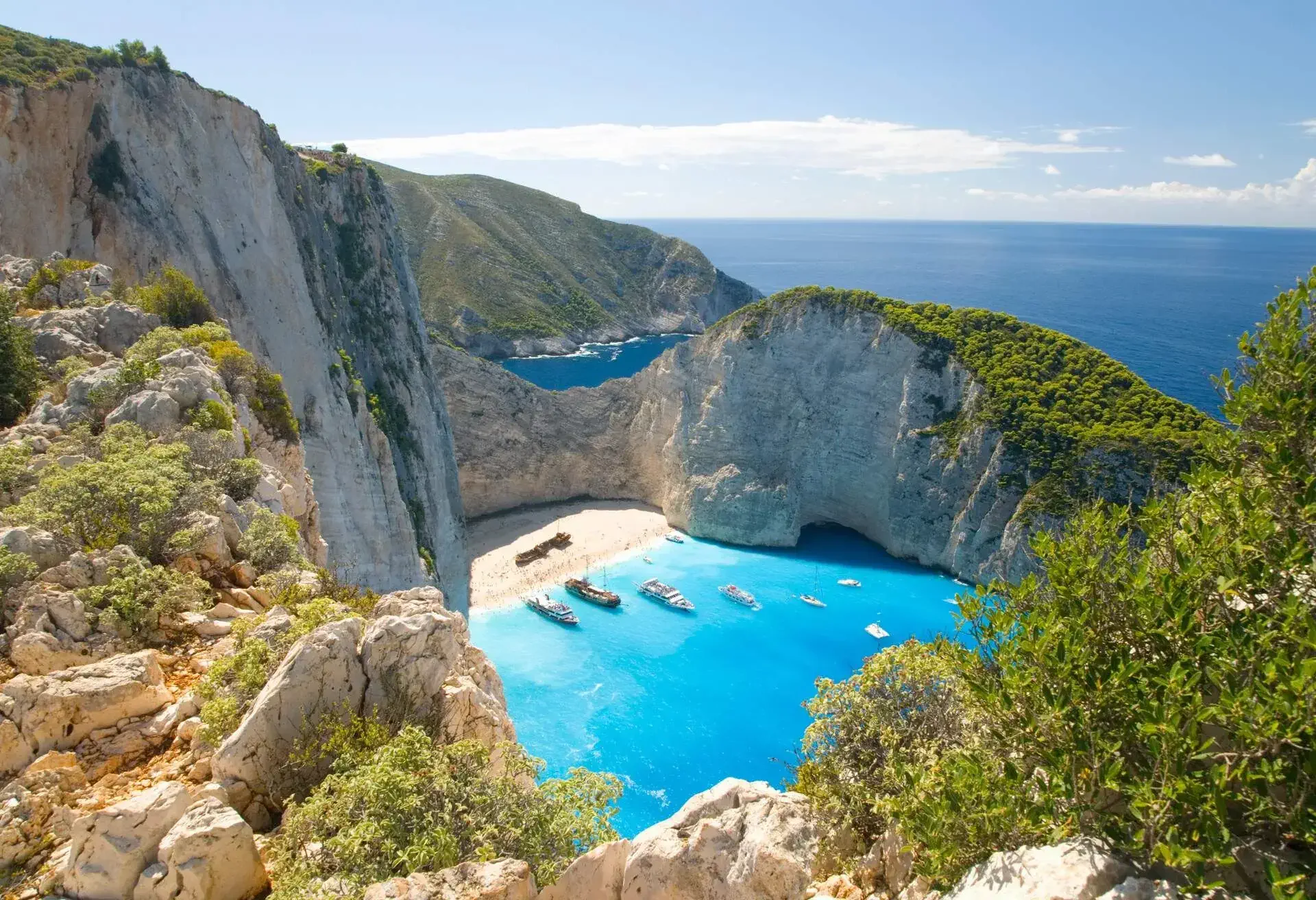 View from clifftop over the turquoise waters of Navagio Bay (aka Shipwreck Bay, Smugglers Cove), pleasure boats anchored off the beach, near Anafonitria, Zakynthos (aka Zante, Zakinthos), Ionian Islands, Greece, Europe.