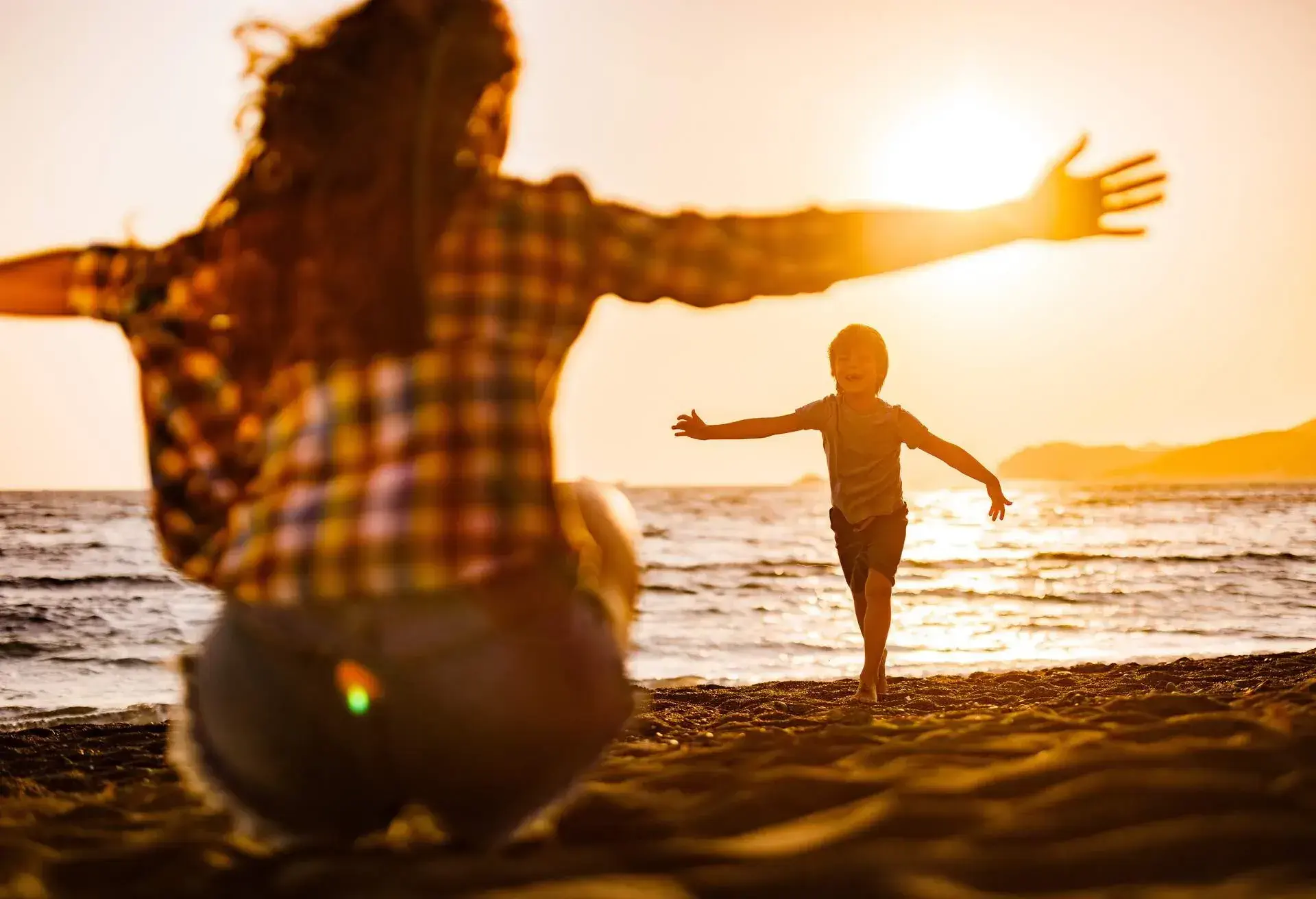Happy little boy having fun while running into his mother's embrace on the beach at sunset.