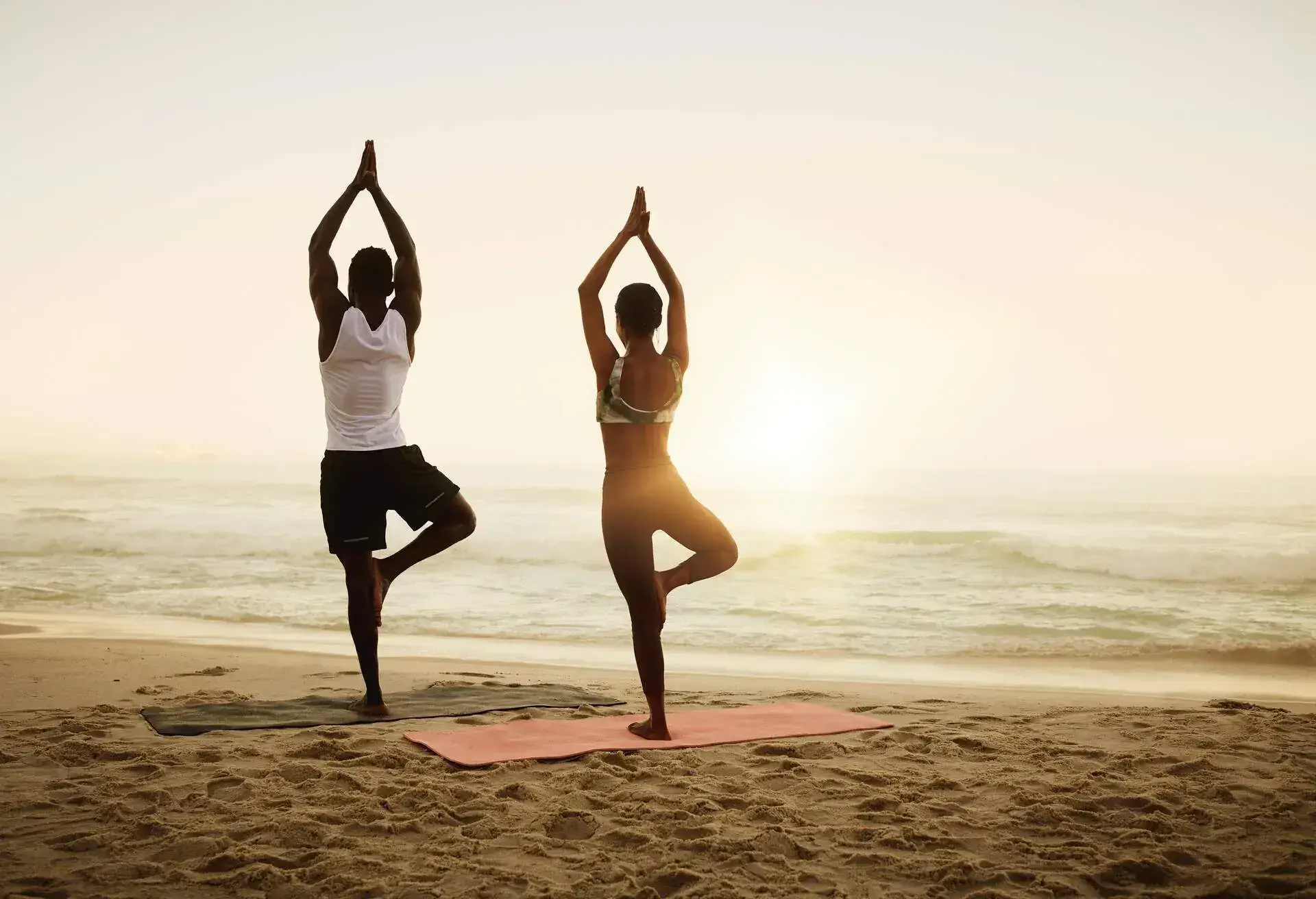 Fit, active and healthy beach yoga people holding tree pose while stretching, balancing or exercising for pilates or meditation by sea or ocean. Calm, serene or zen yogis in holistic sunrise exercise