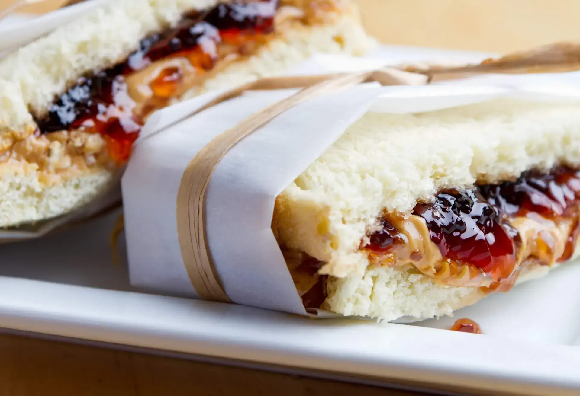 PB&J sandwich wrapped in parchment. Served on a white plate.