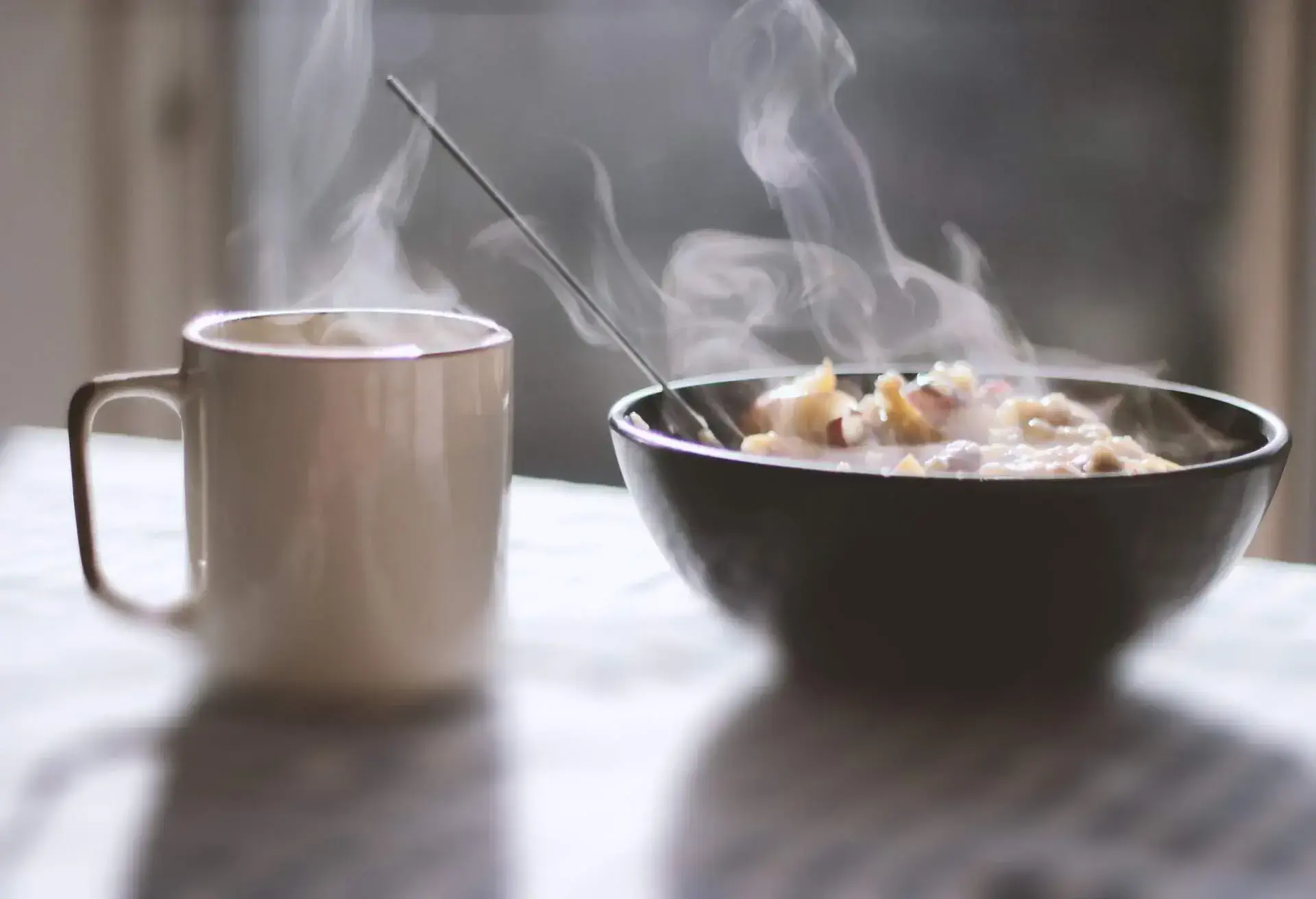Close-up of porridge and tea served in a bowl on table with morning light and shadows coming through the window in the background.