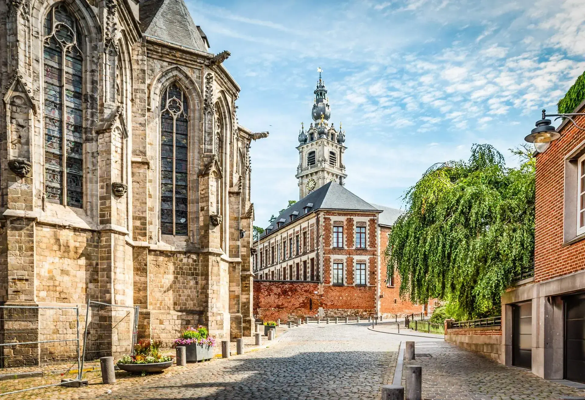 Mons, Hainaut, Wallonia, Belgium. Bright and colorful image with gothic belfry tower and catholic church in city center, cobbled streets and brickstone houses.
