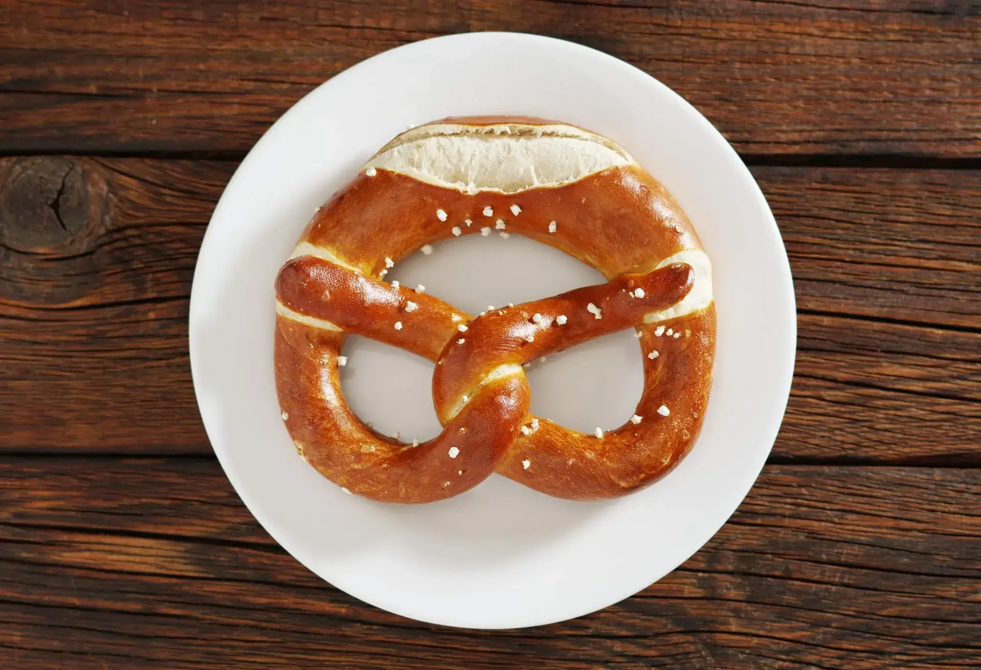 Freshly baked bavarian pretzel on a plate on dark wooden table, top view