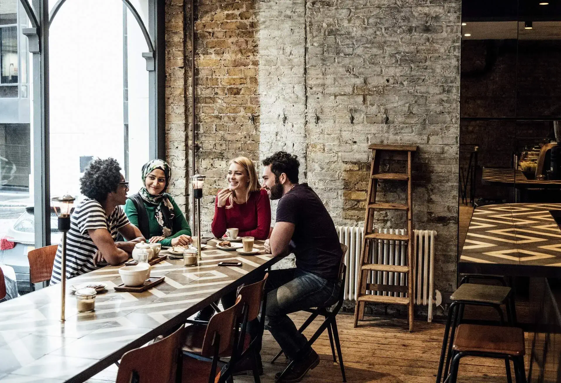 Multi racial group of people talking and smiling in restaurant, man with afro hairstyle talking, man and two women litening