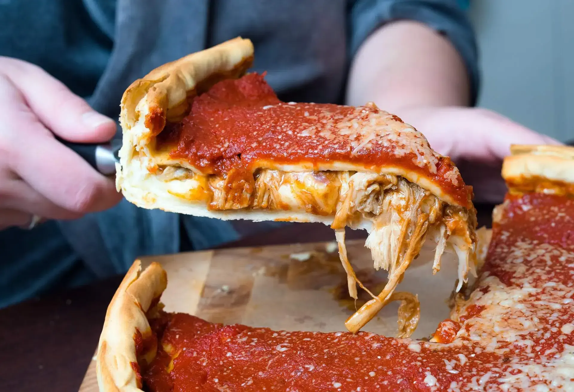 Top view of Chicago pizza. Woman hands cutting Chicago style deep dish Italian cheese pizza with tomato sauce and beef meet inside