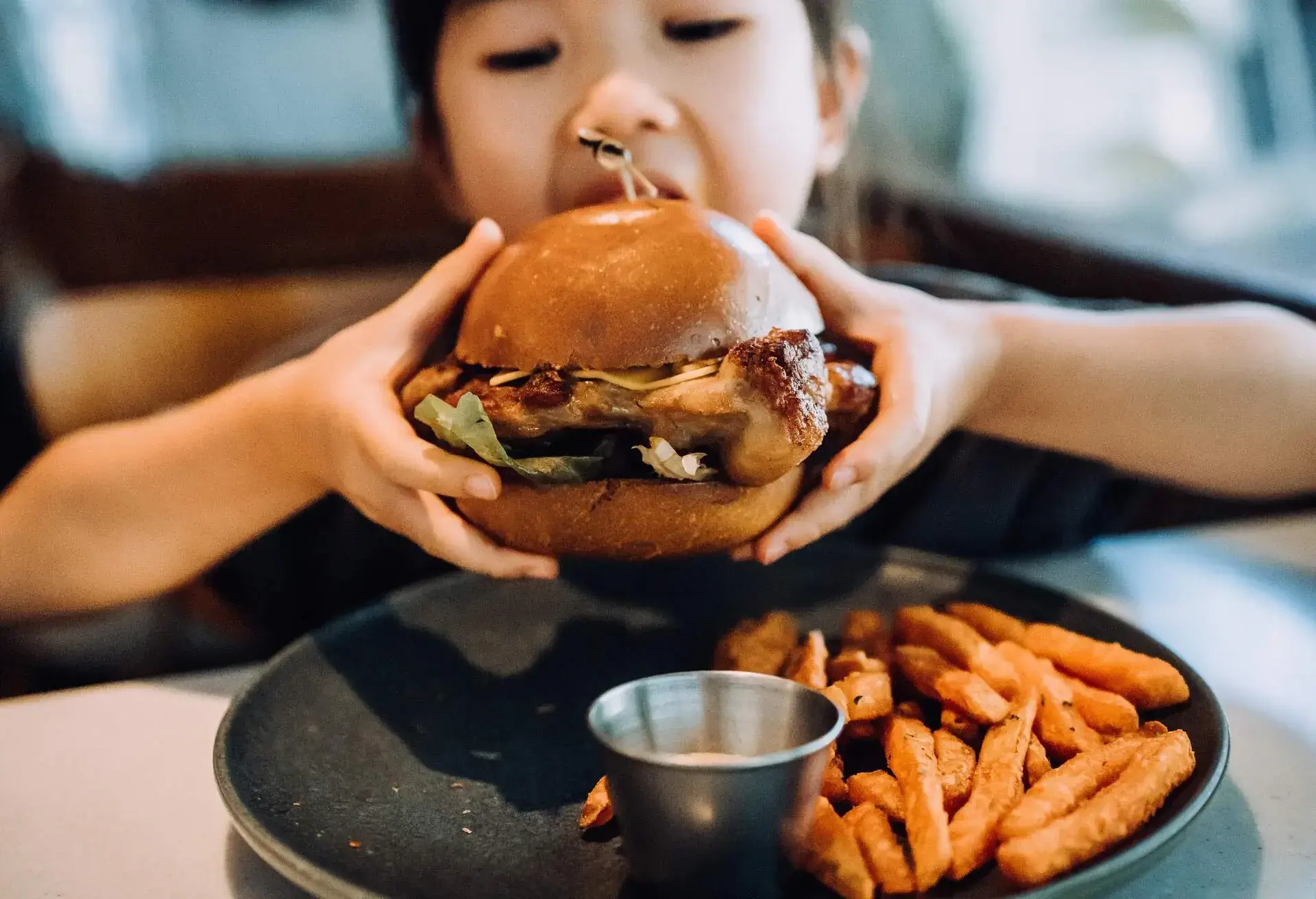 THEME_PEOPLE_KID_GIRL_EATING_BURGER_RESTAURANT_GettyImages-1417351751