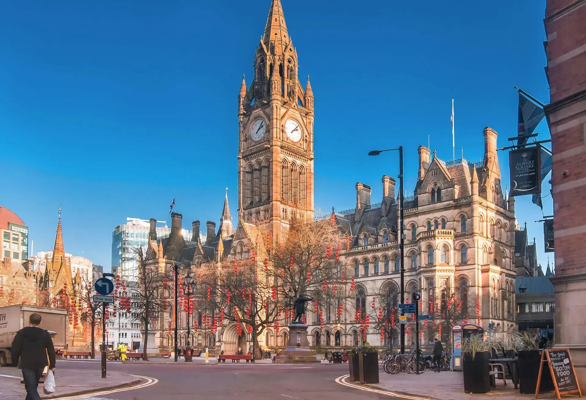 Leafless trees decorated with red lanterns in front of the Manchester Town Hall.