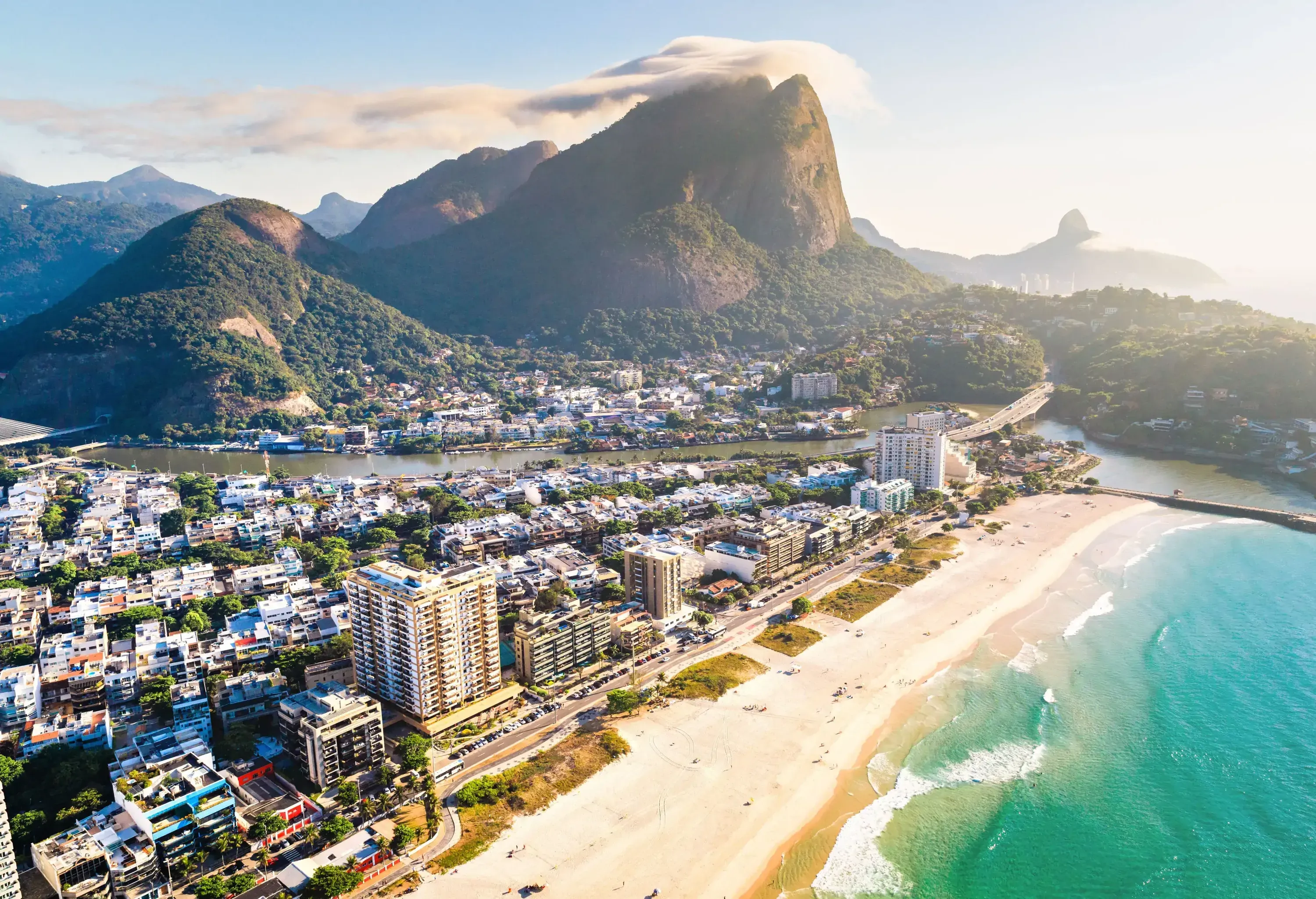 Buildings elegantly line the picturesque beach, framing a bustling cityscape, while a towering mountain with a steep peak rises majestically in the background.