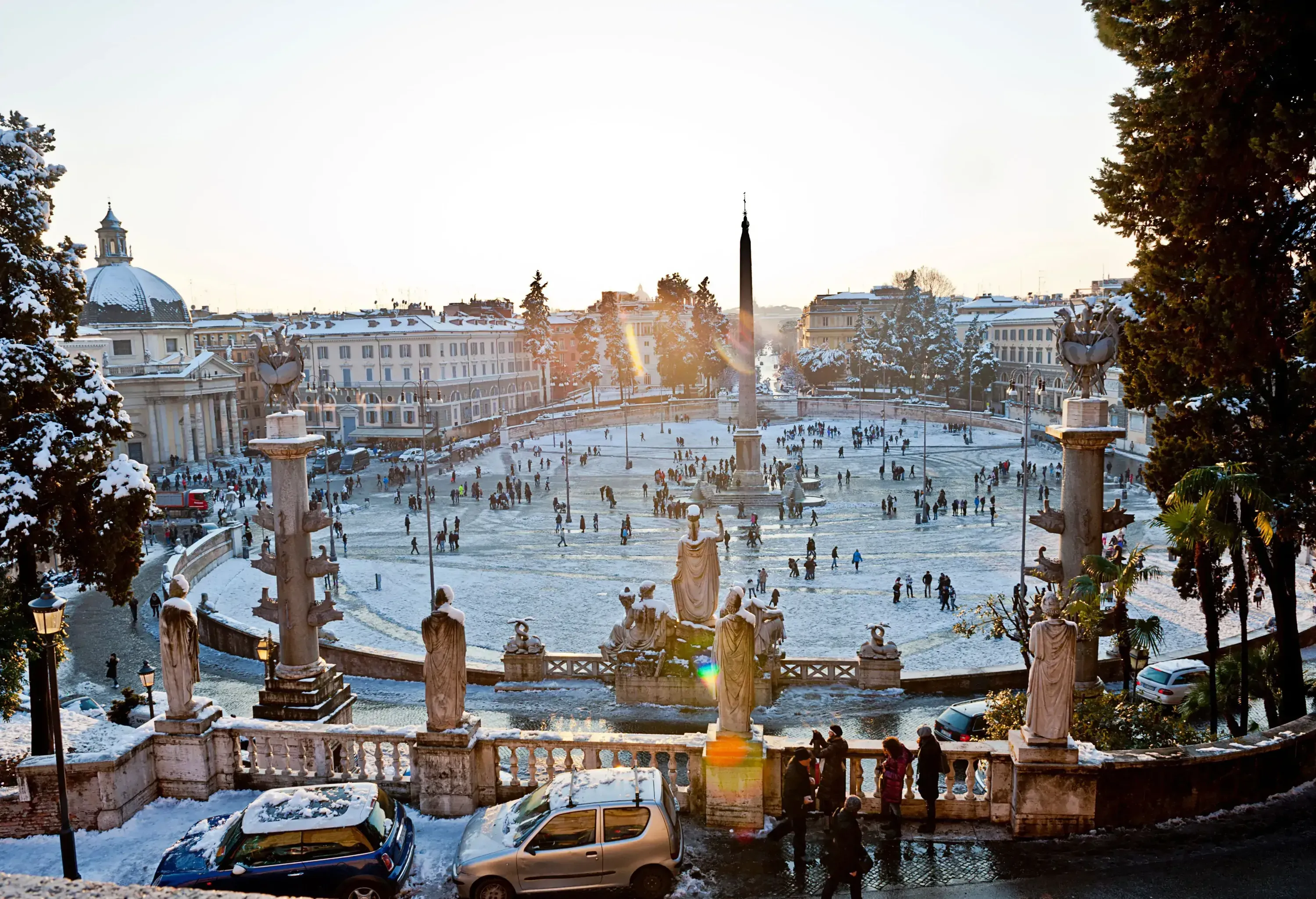 A bustling snow-covered public square surrounded by historic buildings and trees under a bright sky.