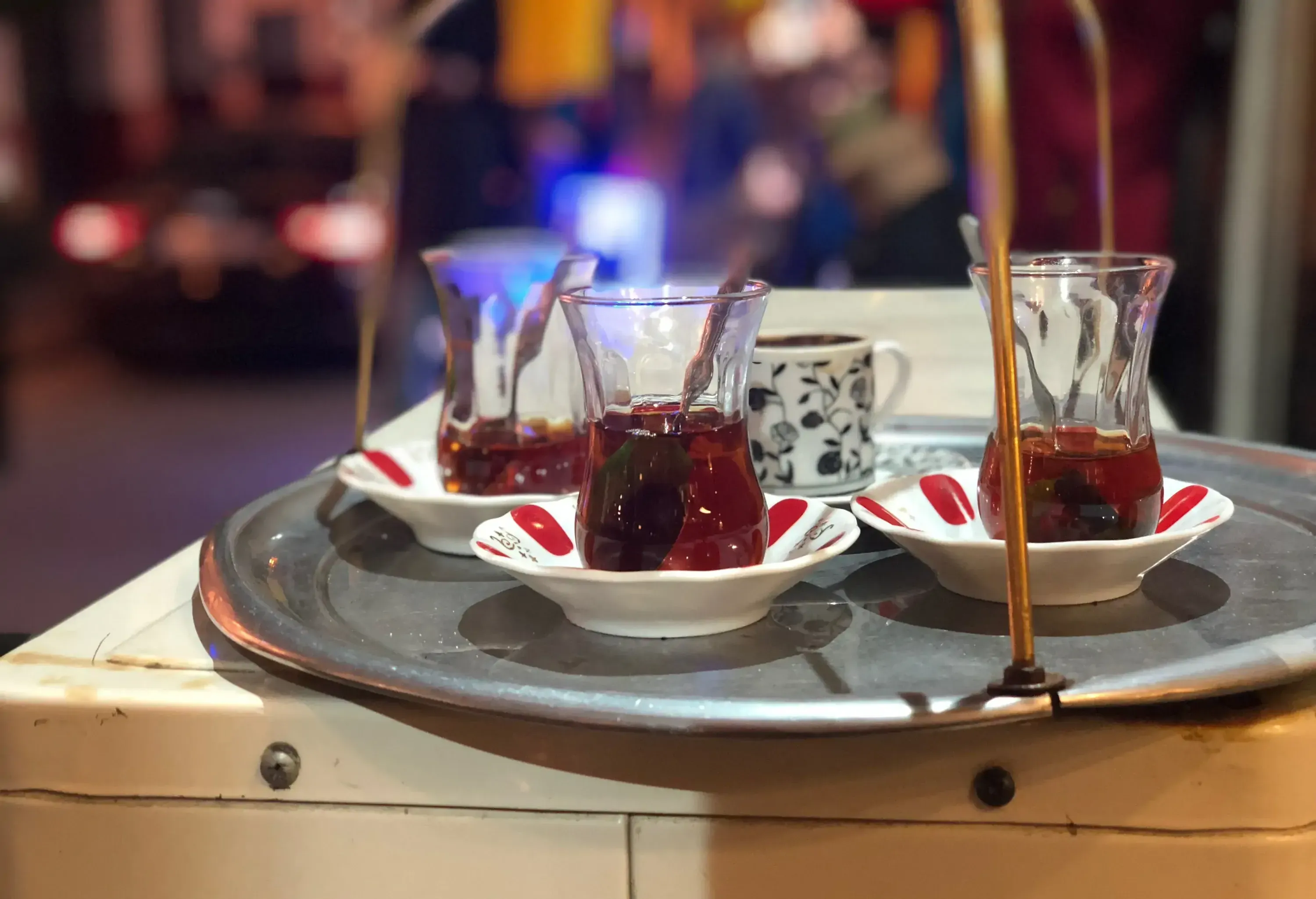 A cup and three glasses of tea on small plates served on a silver platter.