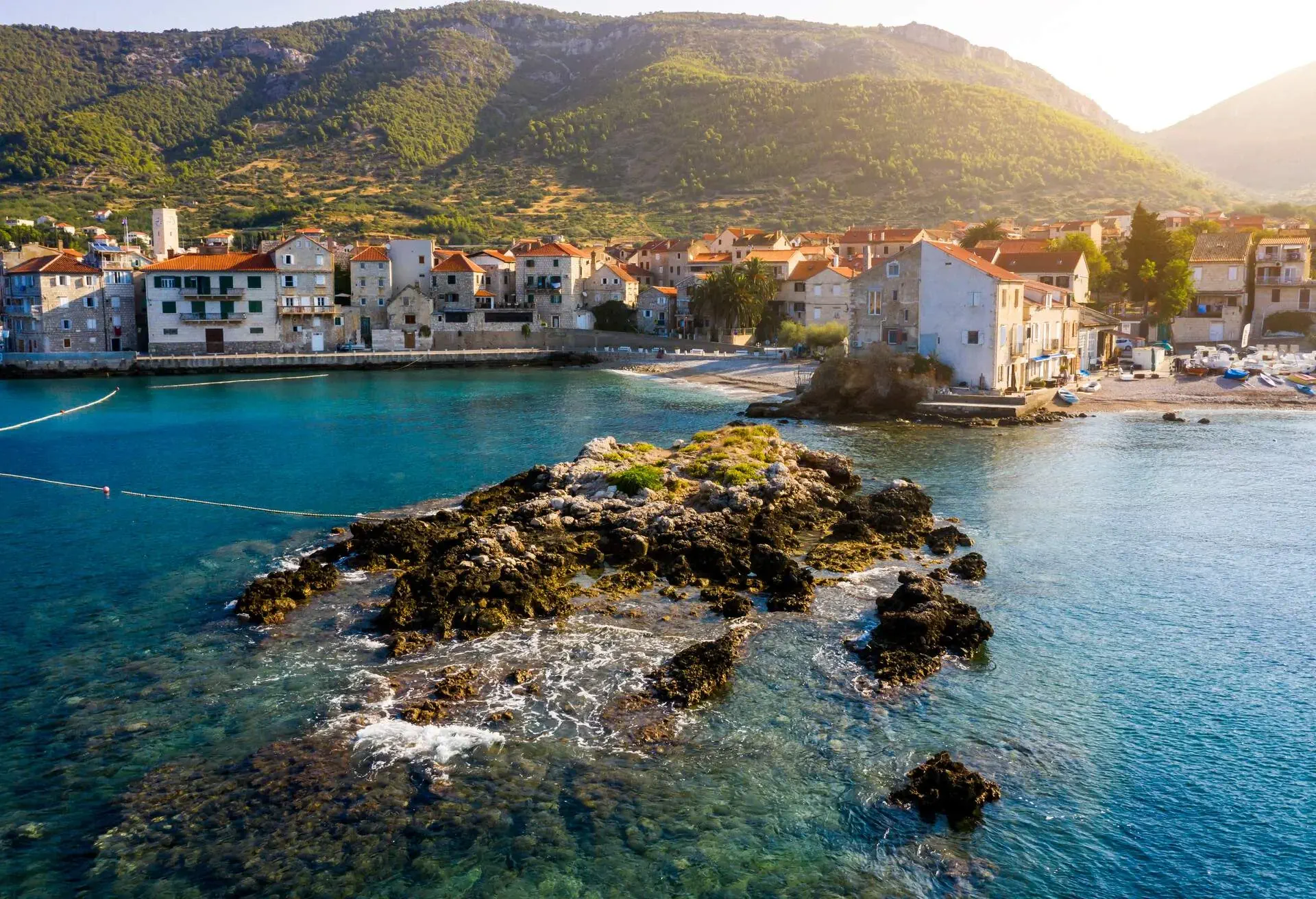A coastal town lying at the foot of a hill surrounded by clear turquoise waters.